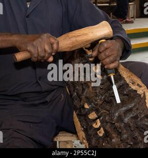 Karatu, Tanzania - 16th ottobre 2022: Un uomo che intagliava il legno, usando uno scalpello e un mazzuolo. Foto Stock