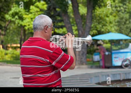 Kiev, Ucraina - 06 2018 luglio: Musicista che suona con la sua tromba in un parco pubblico. Foto Stock