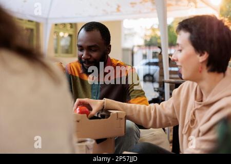 Il cliente maschio mordere la mela al festival di prova dell'alimento durante l'autunno, i clienti che hanno divertimento con i proprietari dello stand del mercato degli agricoltori. Giovani che si godono di bio-prodotti biologici, provando un assaggio di frutta e verdura. Foto Stock