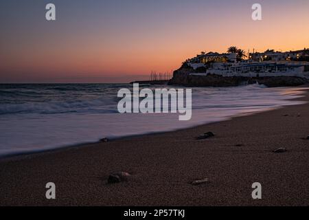 Spiaggia e mare calmo al tramonto con cielo dorato, viola e rosso. Un viaggio lungo la costa catalana della Spagna. Spiaggia Garraf al tramonto, mare mediterraneo Foto Stock