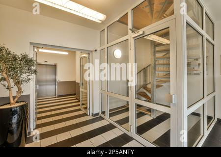 un corridoio con pavimento a scacchi bianco e nero, porte in vetro si aprono per rivelare un ingresso nell'edificio Foto Stock