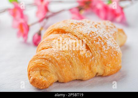 Croissant con caramelle allo zucchero, colazione tipica del mattino. Sfondo bianco e fiore rosa Foto Stock