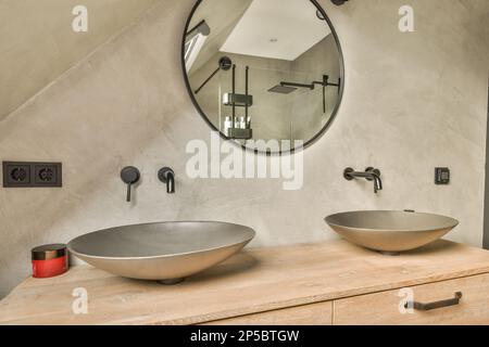 due lavandini posti sopra un tavolo di legno accanto ad un grande specchio rotondo nell'angolo di un bagno Foto Stock