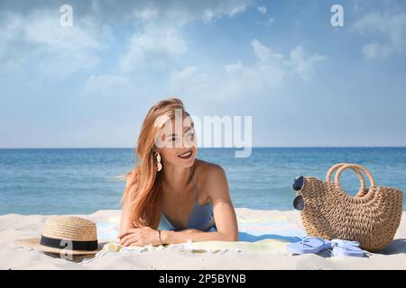 Bella donna con borsa e altri articoli da spiaggia sulla sabbia vicino al mare Foto Stock