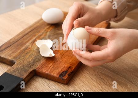 Donna che sbuccia l'uovo bollito al tavolo di legno, primo piano Foto Stock