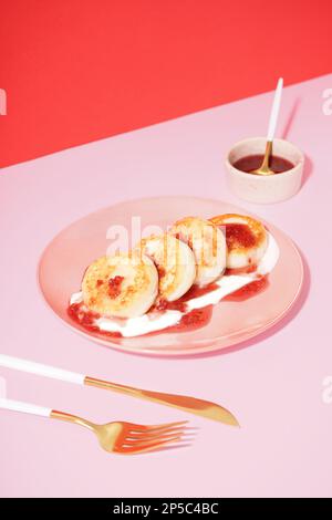 Piatto di gustosi pancake al formaggio casolare con marmellata di lamponi e panna acida sul tavolo rosa Foto Stock