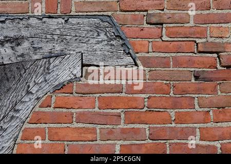 Primo piano di vecchio muro di mattoni rossi che ha linee orizzontali irregolari e fa parte di un'annata, telaio della porta di legno sul lato sinistro. Foto Stock