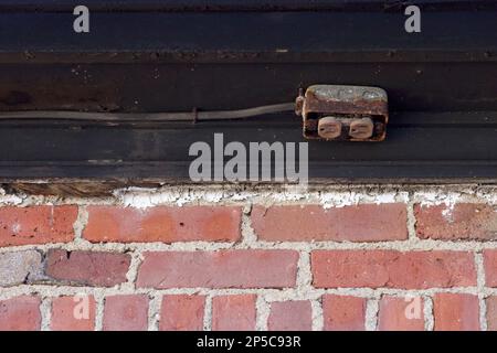 Parete in mattoni rossi con rivestimento nero sulla parte superiore, con presa elettrica arrugginita installata sul rivestimento. È stato alterato dall'essere all'aperto nel New England. Foto Stock