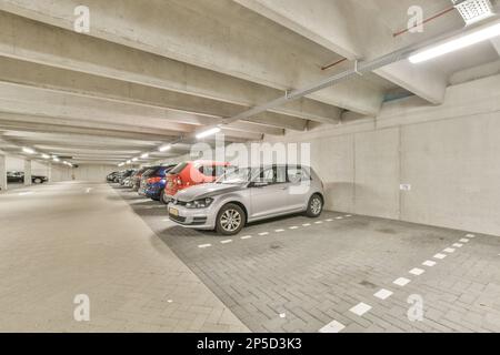 un parcheggio sotterraneo con auto parcheggiate nei garage e persone che camminano sul marciapiede per prendere le loro corse Foto Stock