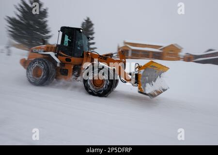 Un trattore giallo con catene per pneumatici passa davanti a una casa in costruzione durante una bufera di neve a Mammoth Lakes, California. Foto Stock