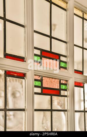una finestra con molti pezzi di vetro colorati e il riflesso nella finestra è bianco, rosso, verde e nero Foto Stock