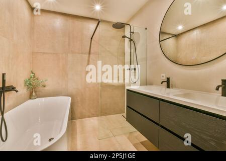 un bagno moderno con piastrelle beige alle pareti e un grande specchio rotondo sopra la vasca nell'angolo Foto Stock