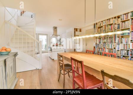 Amsterdam, Paesi Bassi - 10 aprile, 2021: Sala da pranzo con libri sulle pareti e scale che portano al secondo piano in una casa open space Foto Stock