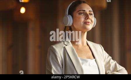 donna d'affari che indossa le cuffie wireless in un ufficio di lavoro. Donna professionale che ascolta musica rilassante al lavoro. Foto Stock