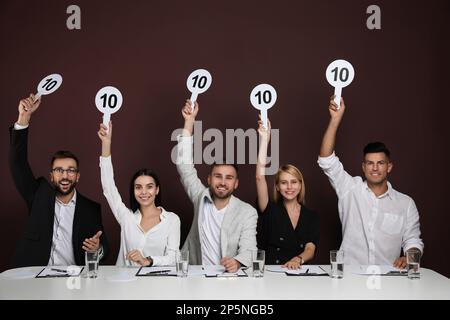 Gruppo di giudici che tiene i segni con il punteggio più alto a tavola su sfondo marrone Foto Stock