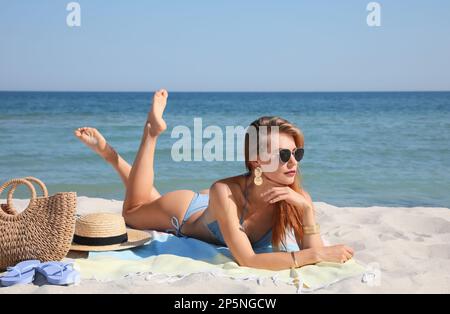 Bella donna con borsa e altri articoli da spiaggia sulla sabbia vicino al mare Foto Stock