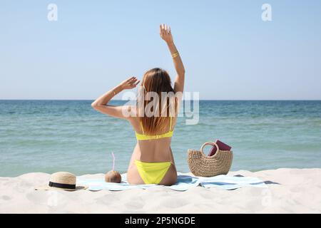 Donna con borsa e altri articoli da spiaggia sulla sabbia vicino al mare, vista sul retro Foto Stock