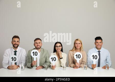 Gruppo di giudici che tiene i segni con il punteggio più alto a tavola su sfondo beige Foto Stock
