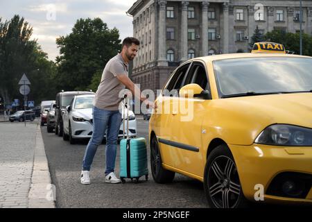 Bel giovane uomo con valigia che si porta in taxi su strada cittadina Foto Stock