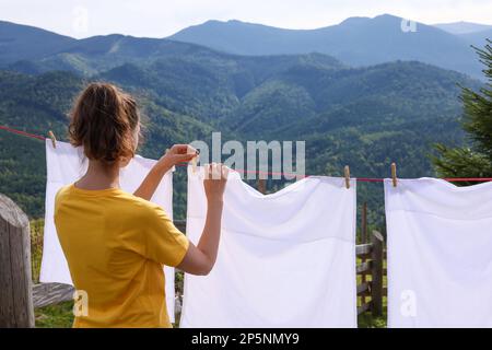 Donna appesa lavanderia pulita con clothespins sulla linea di lavaggio in montagna, vista sul retro Foto Stock