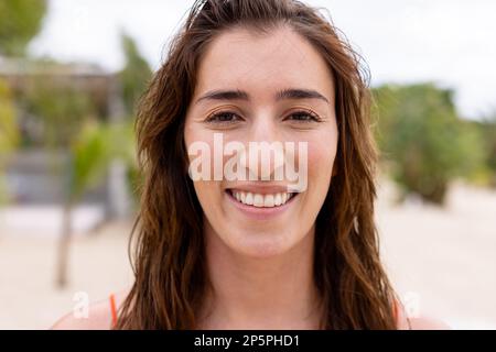 Ritratto di felice donna biraciale guardando la macchina fotografica e sorridendo in spiaggia Foto Stock