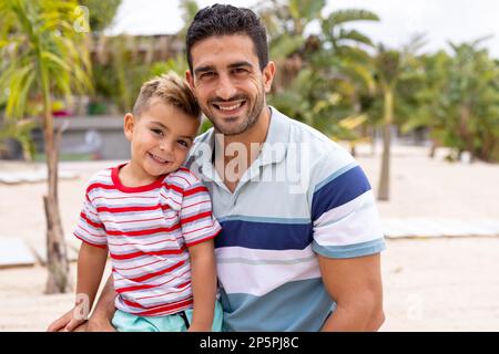 Ritratto di felice padre e figlio biraciale abbracciando e sorridendo in spiaggia Foto Stock