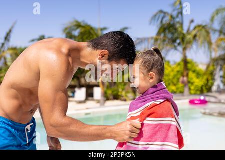 Felice padre e figlia biraciale utilizzando asciugamano presso la piscina Foto Stock