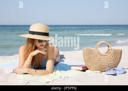 Bella donna con borsa e altri articoli da spiaggia sulla sabbia vicino al mare Foto Stock