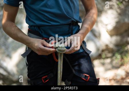 Primo piano di un maschio arrampicatore legato corda e preparandosi a salire Foto Stock