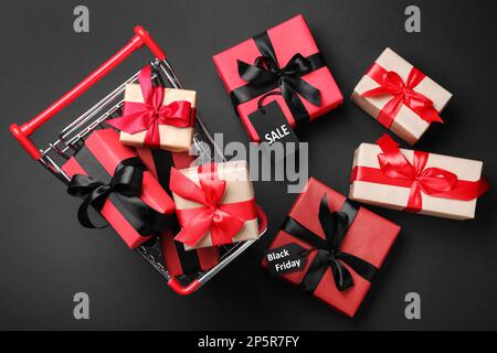 Carrello con scatole regalo su sfondo scuro, piatto. Vendita Black Friday Foto Stock