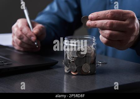 La mano dell'uomo d'affari conta i centesimi sulla sua scrivania dal suo laptop Foto Stock