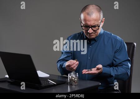 Uomo d'affari maturo alla sua scrivania contando penny, sul bordo del fallimento Foto Stock