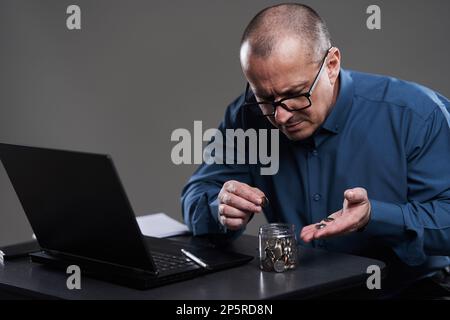 Uomo d'affari maturo alla sua scrivania contando penny, sul bordo del fallimento Foto Stock