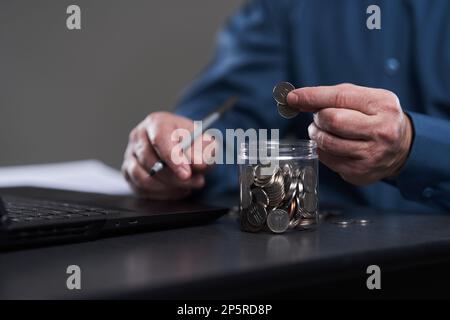 La mano dell'uomo d'affari conta i centesimi sulla sua scrivania dal suo laptop Foto Stock