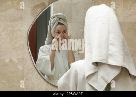 Donna che fa anti massaggio del viso di fronte allo specchio dopo la doccia, concetto di cura della pelle di bellezza a casa Foto Stock