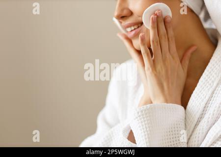 Giovane donna in vestito bianco e asciugamano sulla sua testa strofinare la pelle del suo viso con tamponi di cotone. Pulizia e cura del corpo sana dopo la doccia. Primo piano di Foto Stock