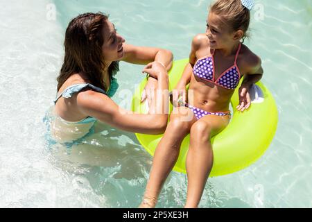 Felice madre biraciale e figlia che giocano insieme in piscina Foto Stock