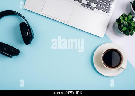 Una tazza di caffè, computer portatile, cuffie e succulente pianta su sfondo blu. Ambiente di lavoro accogliente, concetto di lavoro da casa. Vista dall'alto, disposizione piatta, copia Foto Stock