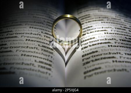 anello d'oro in un libro aperto che oscura un cuore Foto Stock