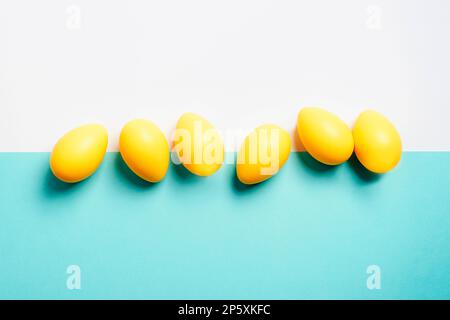 Uova di Pasqua gialle su sfondo bianco e blu. Vista dall'alto, disposizione piatta, spazio di copia. Foto Stock