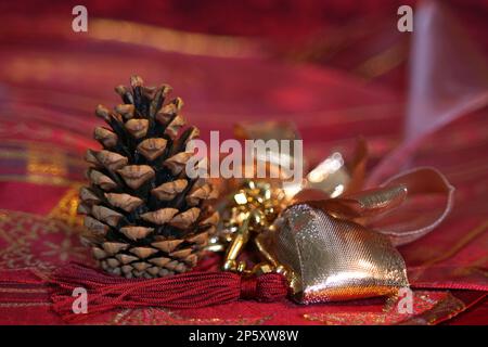 Cono di pino con nastro dorato su sfondo rosso, decorazione natalizia Foto Stock