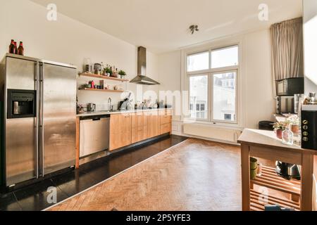 una cucina moderna con armadietti in legno ed elettrodomestici in acciaio inossidabile in camera è ben illuminata dal sole che splende attraverso la finestra Foto Stock