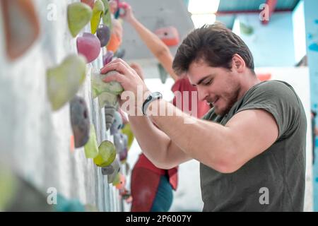 Sport arrampicata indoor sicuro in arrampicata parete. Bouldering l'iniziazione dell'uomo Foto Stock