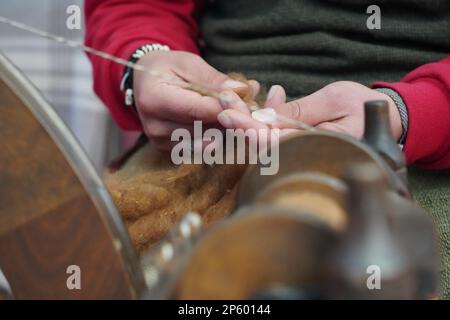 Un artista di strada che produce cucire con ruota di filatura tradizionale. Fibra artigianale cucita con macchina d'epoca. Foto Stock