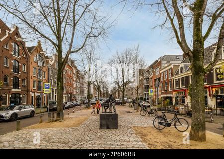 Amsterdam, Paesi Bassi - 10 aprile, 2021: Una strada cittadina con molti edifici e biciclette parcheggiate sui marciapiedi di fronte a un altro edificio in mattoni, alcune persone sono a piedi Foto Stock