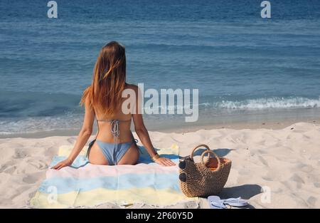 Donna con borsa e altri articoli da spiaggia sulla sabbia vicino al mare, vista sul retro Foto Stock