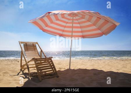 Sedia a sdraio vicino a ombrellone a strisce rosse e bianche sulla spiaggia sabbiosa Foto Stock