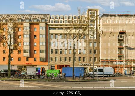 alcuni edifici con biciclette parcheggiate sulla strada di fronte a loro e persone che camminano lungo la strada fino alle loro auto Foto Stock