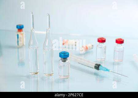 una siringa con ago e fiale di liquido su sfondo blu non riflettente. Il concetto di vaccinazione e medicina. immunizzazione, Foto Stock