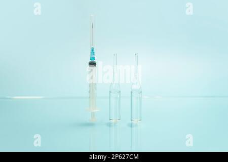 una siringa e fiale di vetro con un liquido trasparente su sfondo blu. il concetto di medicina e salute. Foto Stock